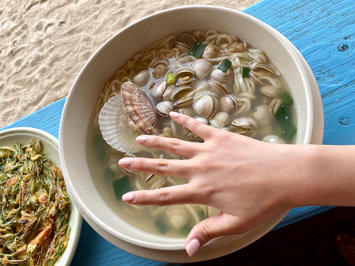 One hand barely covering the large bowl of Haeundae Haemul Kalguksu in Gijang, Busan