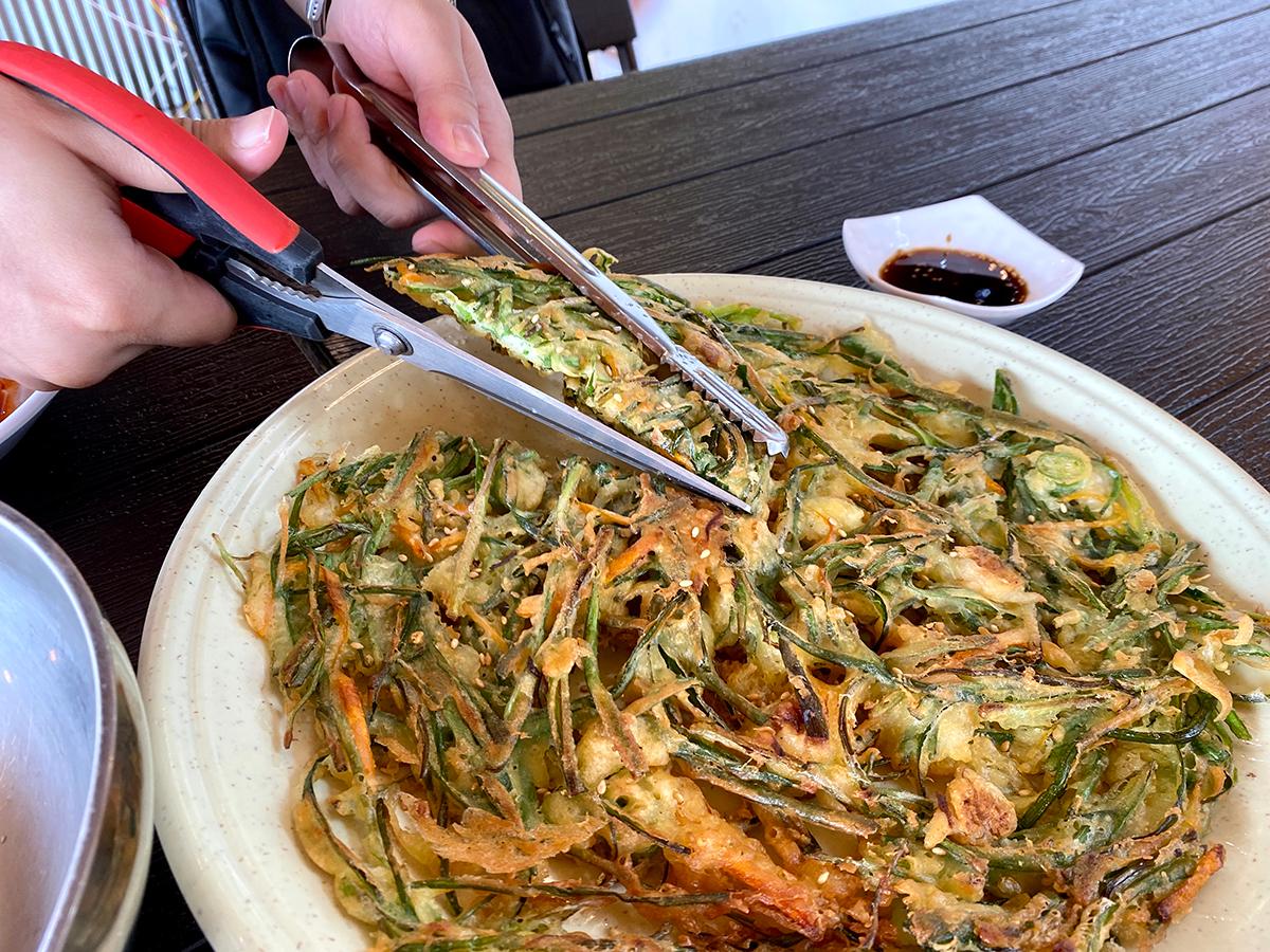 Cutting the chive pancake with tongs and scissors at Haeundae Haemul Kalguksu in Gijang, Busan