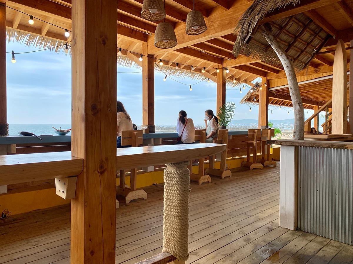 Customers sitting on the wooden bar chairs looking towards the blue ocean in Gijang, Busan