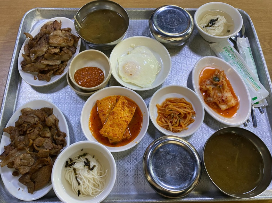 韓国の運転手食堂で提供される典型的な韓国料理セット。豚肉炒め、キムチ、豆腐料理、卵焼き、お味噌汁など、多彩な韓国料理のバリエーション。