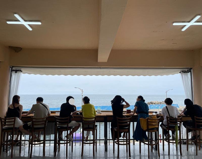 海を眺めながらカフェでリラックスする人々、韓国の海辺カフェでのリラクゼーションタイム