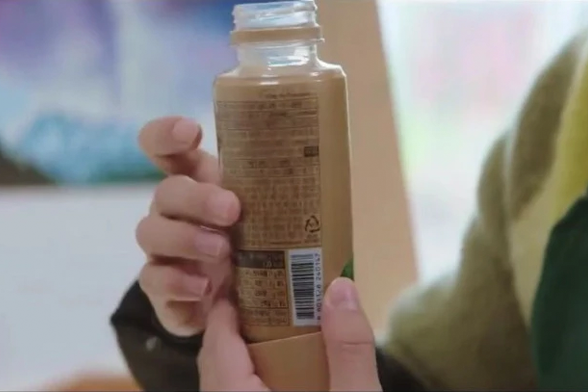 一個男人的手拿著一瓶熱可可飲品，瓶身上印有BTS的圖案。