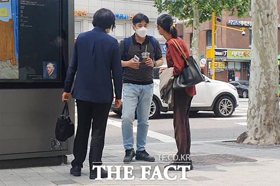 图片中显示三人站立在街头，正在交谈，其中一人手持饮料。