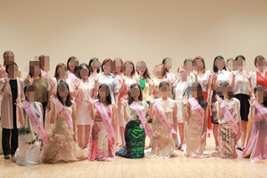 一群人在室内舞台上站成一排，穿着各种礼服和挂着绶带。