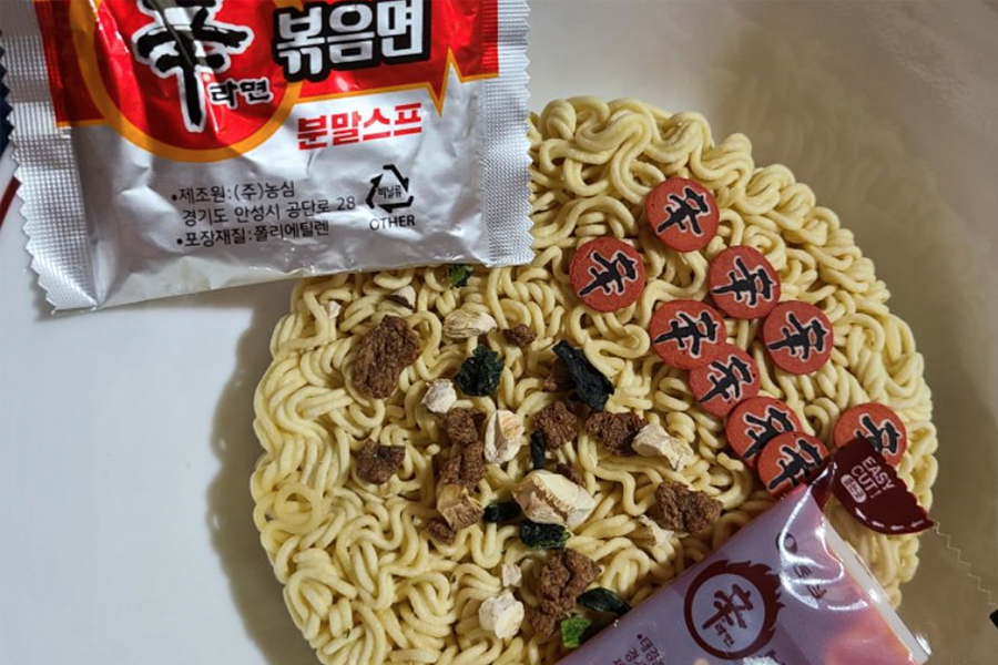 辛拉麵炒麵的特寫圖片，覆蓋著辛味的麵條和印有辛字樣的魚板，展示其鮮美的辛辣口感。