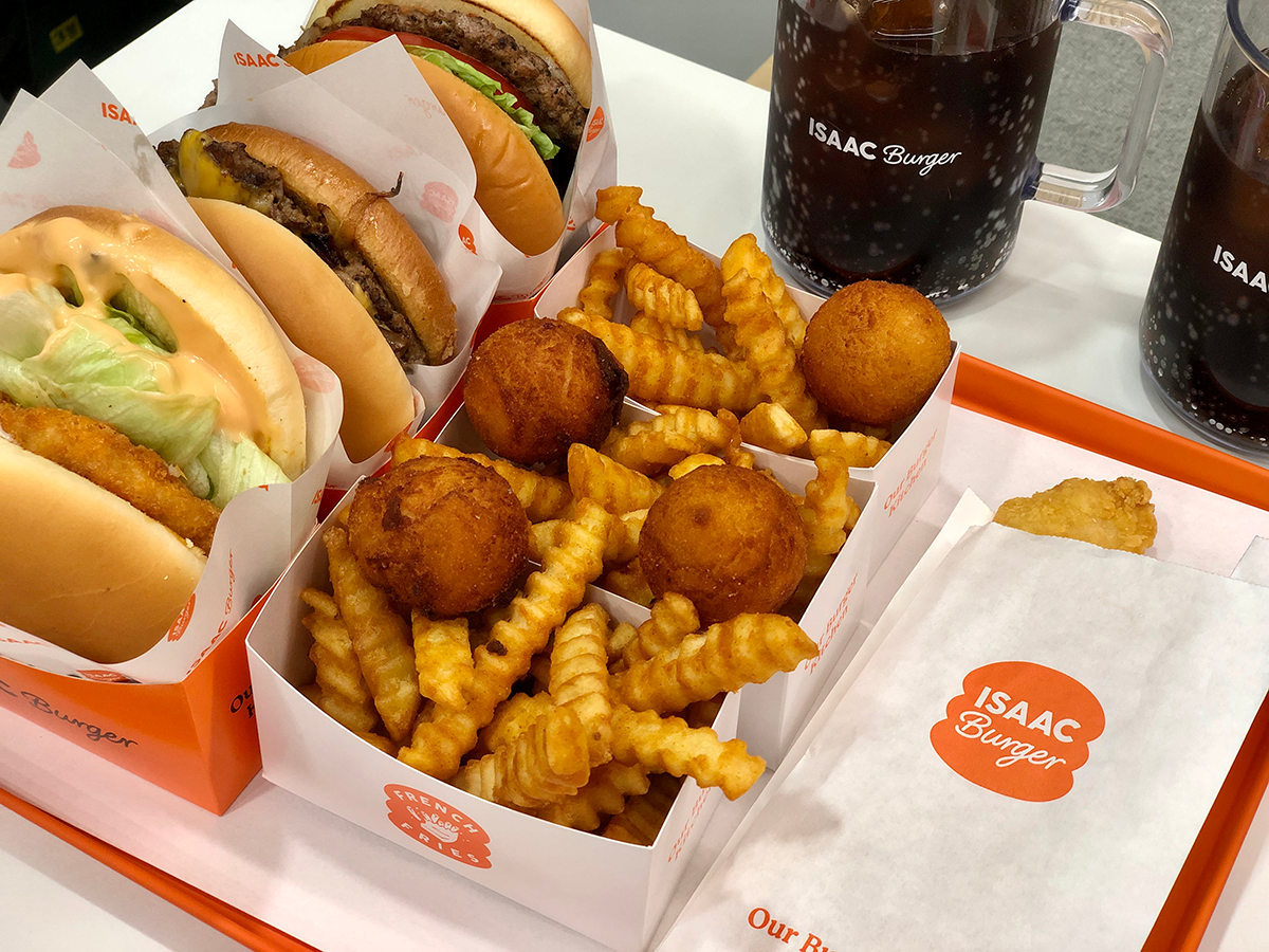 ISAAC Burger fries and cheese balls on an orange tray with burgers and coke drinks surrounding them