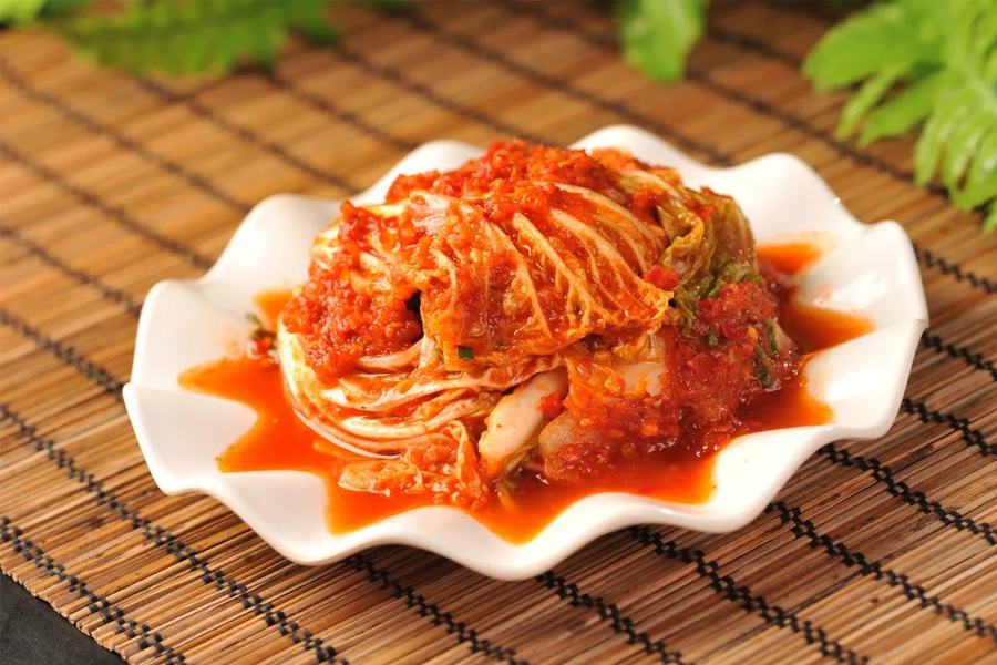 韓式泡菜（Kimchi）在白色平盤上，背景有綠色葉子，顯示傳統韓國泡菜的視覺美。