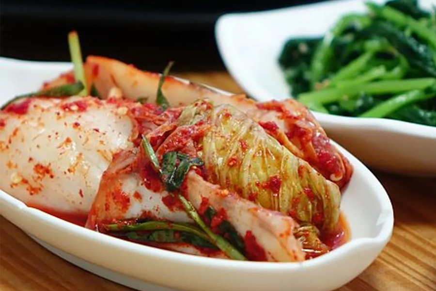 韓式泡菜（Kimchi）與綠色蔬菜的搭配，放置於淺色的陶瓷碟上，強調韓國傳統美食的和諧。