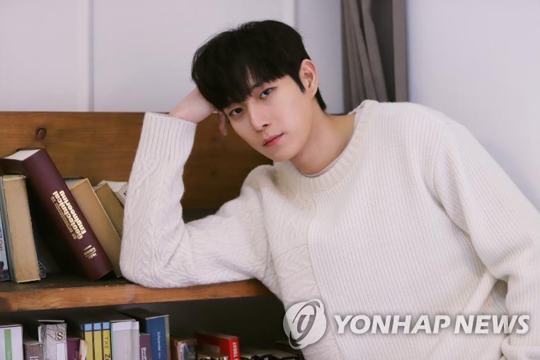 本棚に寄り掛かっている白いセーターを着た俳優キム・ヨンデ