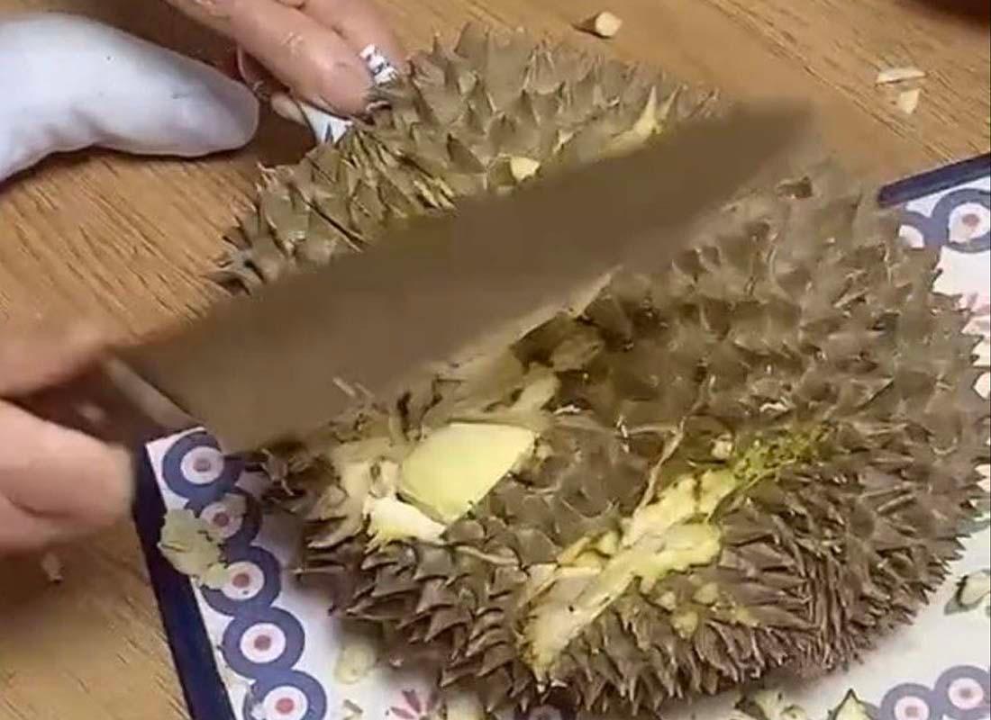 มือสองข้างกำลังใช้มีดตัดเปลือกทุเรียนบนเขียงเพื่อให้สามารถแกะเนื้อทุเรียนออกมาได้