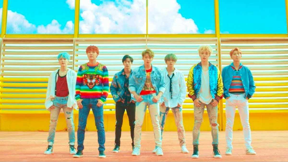 韓國知名男子團體站在色彩繽紛的舞臺上，穿著華麗服裝，演示K-pop音樂風格的視覺衝擊。