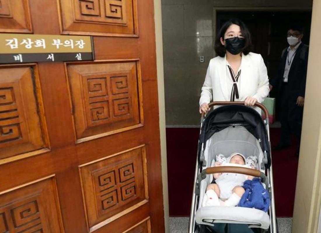 นักการเมืองหญิงในเกาหลีที่ใช้รถเข็นเด็กเดินผ่านประตูเข้าสู่ห้องประชุมในสภา ภาพนี้แสดงถึงความพยายามที่จะรวมการเลี้ยงดูที่บ้านและการมีบทบาทในงานเข้าด้วยกัน