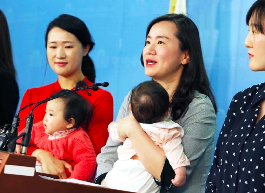 กลุ่มนักการเมืองหญิงเกาหลีที่ยืนอยู่บนแท่นแถลงข่าวพร้อมลูก ๆ ของพวกเธอในงานแถลงข่าว ภาพเน้นถึงความสำคัญของการให้สิทธิสตรีในการมีบทบาททางการเมืองและในครอบครัวอย่างเท่าเทียม