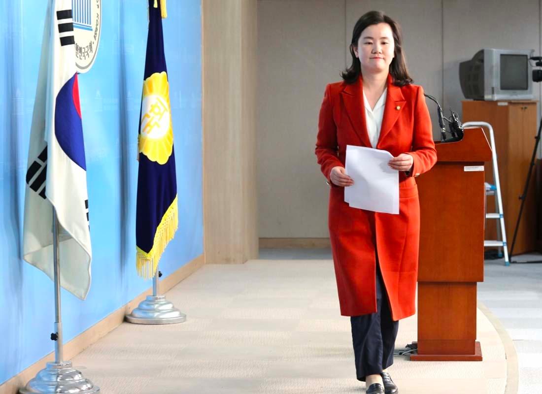 นักการเมืองหญิงสวมชุดสีน้ำตาลและถือเอกสารยืนที่แท่นแถลงข่าวในเกาหลี การปรากฏตัวของเธอเป็นสัญลักษณ์ของการมีส่วนร่วมในรัฐสภา