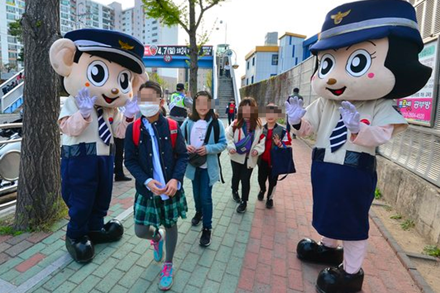 穿着韩国警察吉祥物服装的人物在街上与路人互动，孩子们围绕在吉祥物旁，场景充满欢乐气氛。