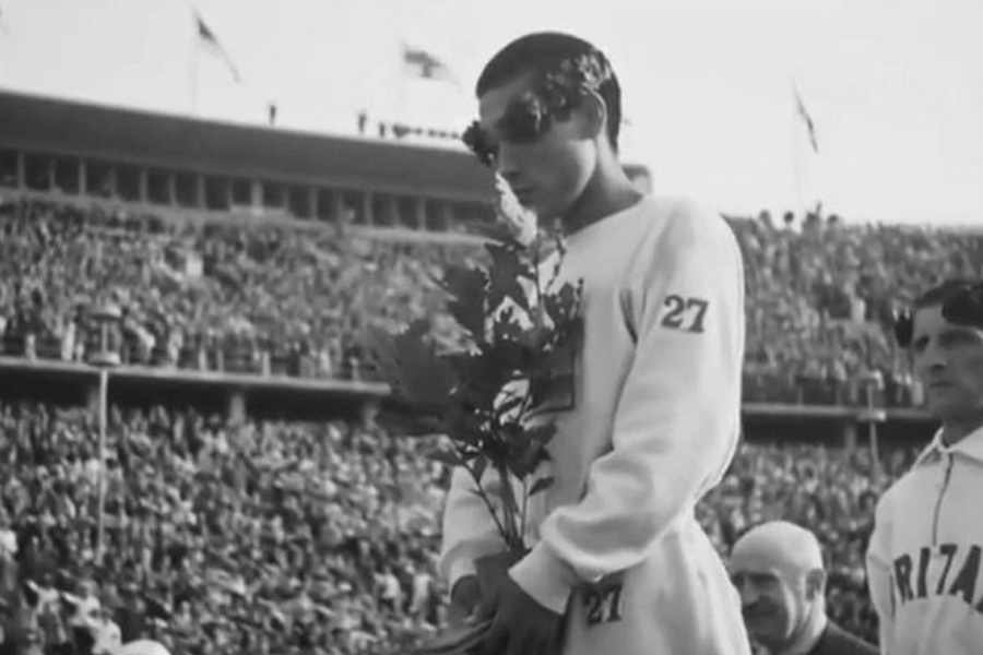 运动员在领奖台上手捧奖杯，低下头，神情复杂。