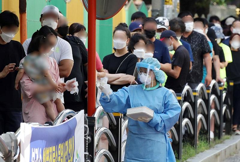 韓国、コロナウイルスの検査場で保護装備を着用している医療スタッフと列に並ぶ人々。