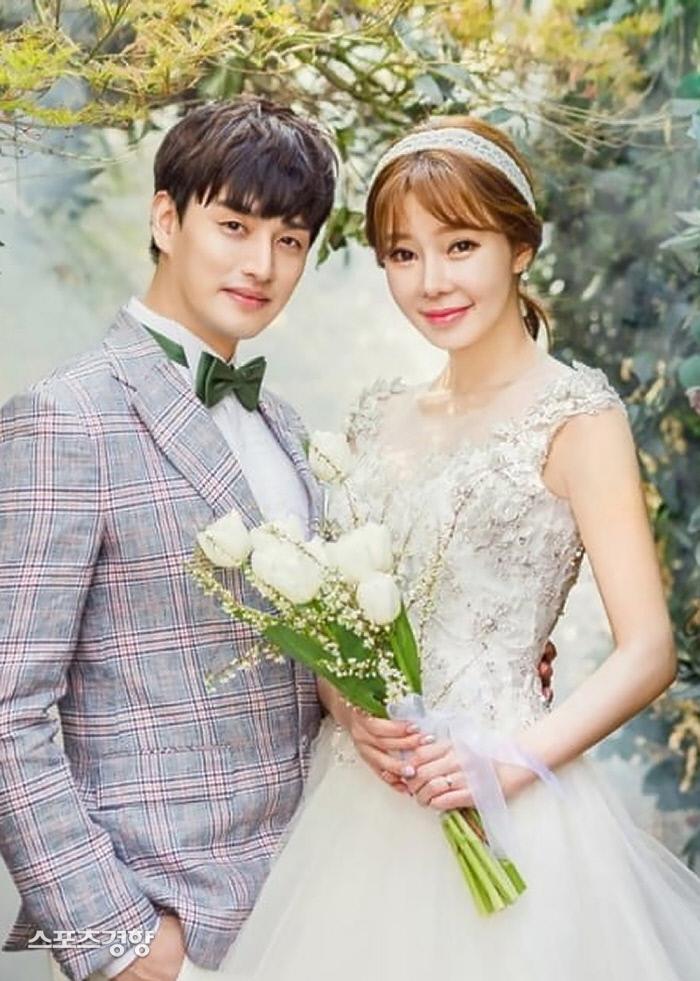 韓国の有名人チ·ヨンスとイライの結婚当時の写真。チ·ヨンスは白いウェディングドレスを着ており、イライはチェック柄のスーツを着ています。2人は愛の象徴として白い花のブーケを持っています。