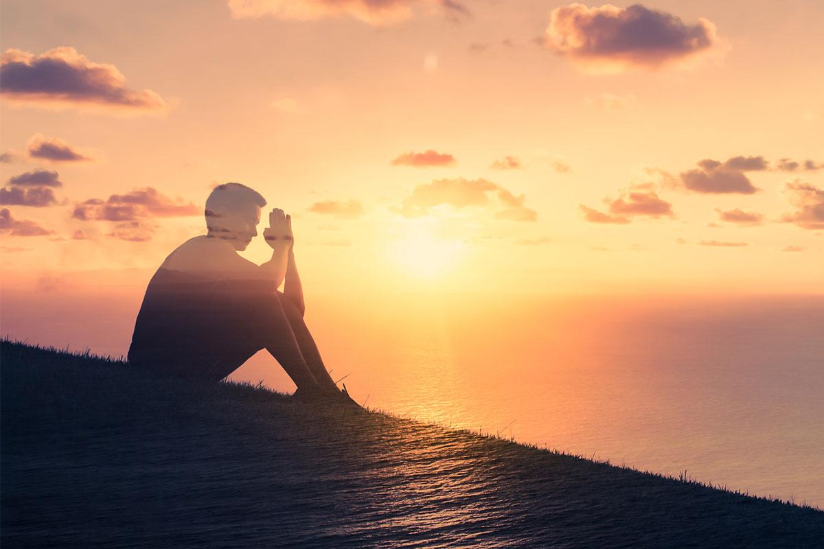 silhouette of a man sitting on the grass and praying