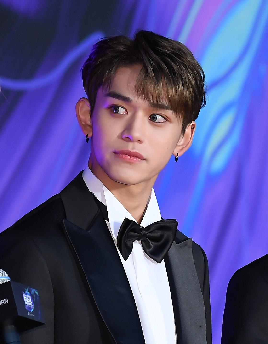 NCTのメンバーがスーツを着ている写真、マイクが置かれた記者会見場の風景