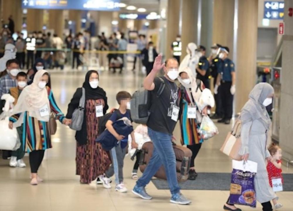 Afghan refugee families arriving at Incheon International Airport, carrying belongings and guided by airport staff.