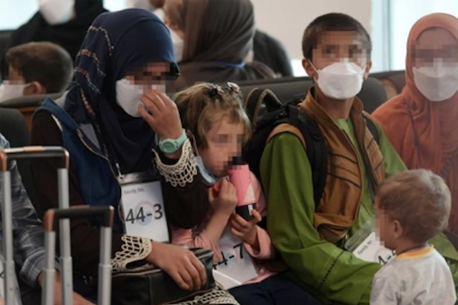 阿富汗难民家庭在机场休息区等待，很多儿童坐在椅子上，手拿着随身物品。