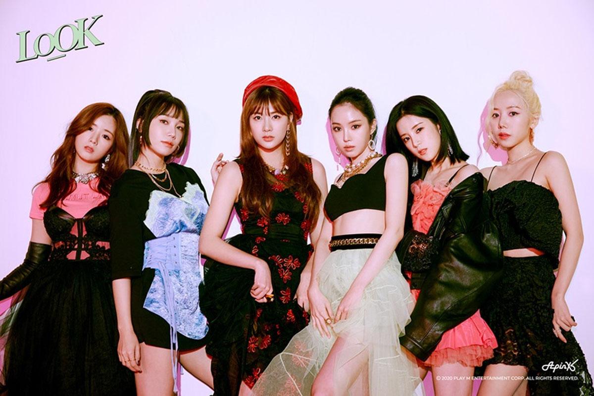 韓國女團 Apink 穿著華麗的舞台服裝，背景是粉色調燈光，展現出優雅且活潑的氛圍。