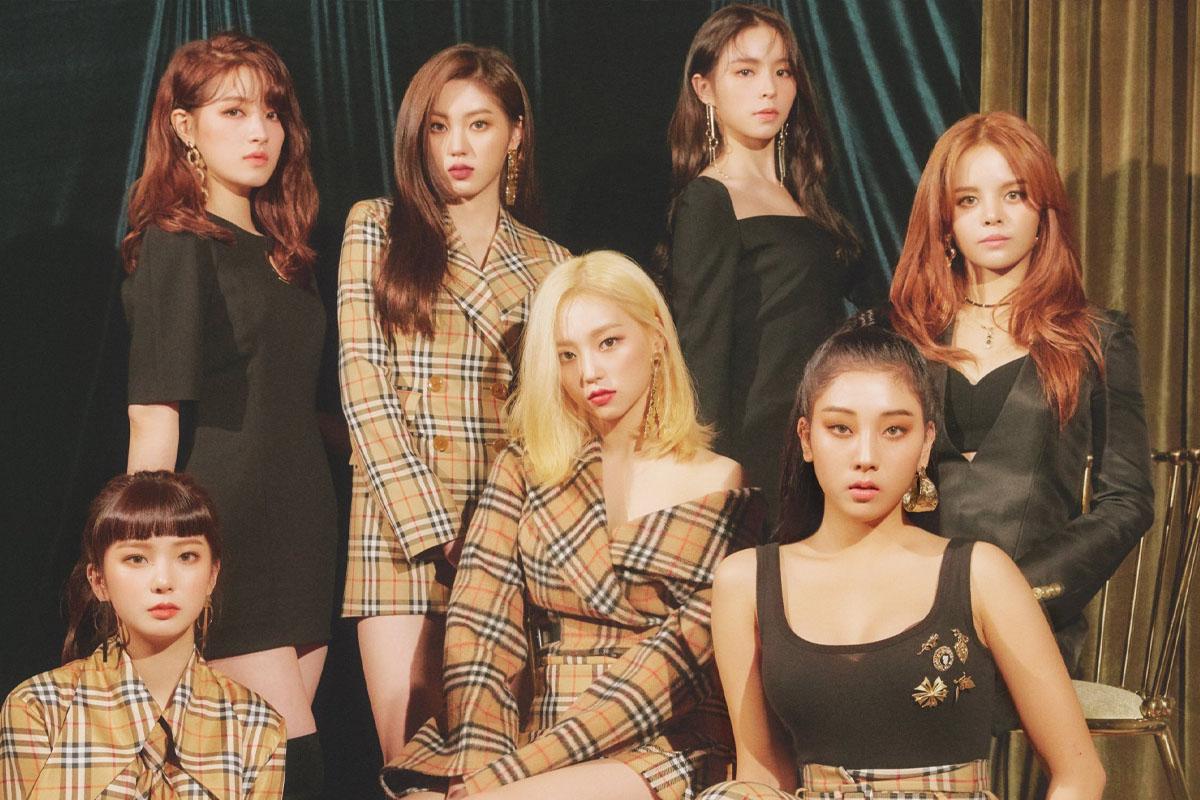 韓國女團 CLC 的成員穿著時尚服裝，站在舞台前，背景是暗綠色的絲綢簾，氣氛高雅神秘。