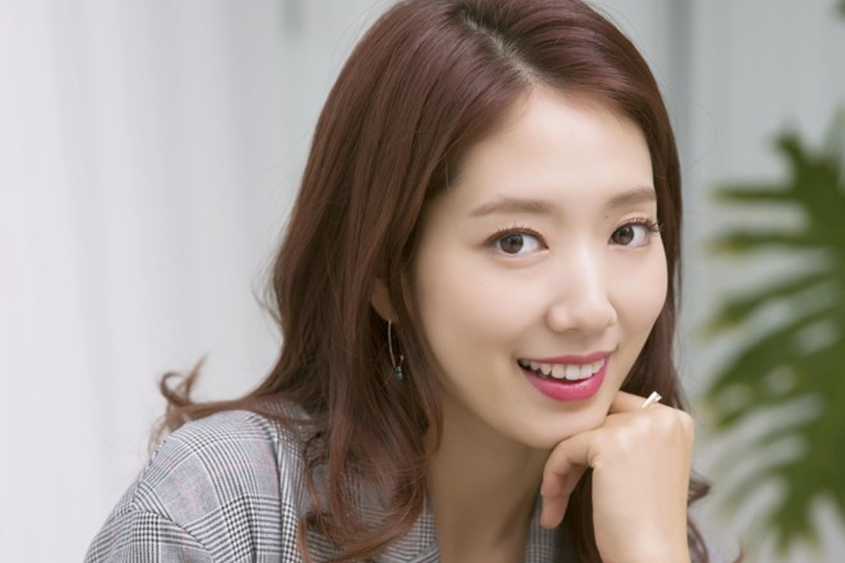 韓國女演員，戴著耳飾，穿著灰色格紋外套，面部模糊，右手託著下巴，背景模糊不清