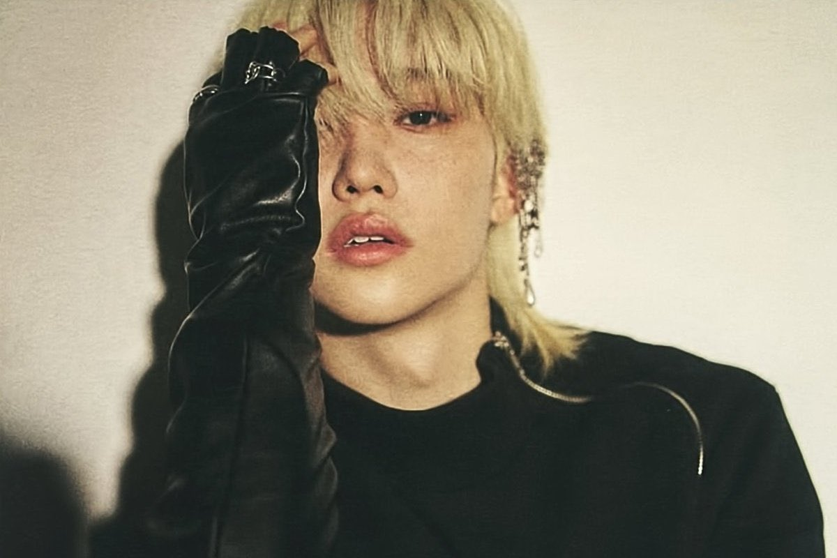 韓國知名男偶像身穿黑色皮衣，側臉模糊不清，背景為暖色調，呈現時尚酷炫風格