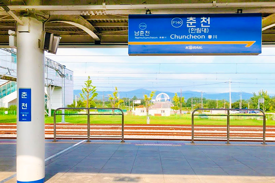 江原道春川車站的風光，展示從站臺看到的火車軌道和遠處的綠色風景。