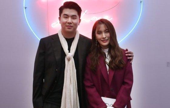 ネオンサインを背景にして、スカーフを巻いたスーツ姿の人物とマゼンタ色のコートを着た人物が立っている様子。韓国芸術イベントにて。