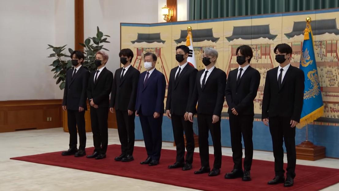 BTSメンバーが大統領特別使節の任命を受けるために大統領と一緒に青瓦台で撮影。背景には韓国の伝統的な絵と大統領の旗が飾られている。