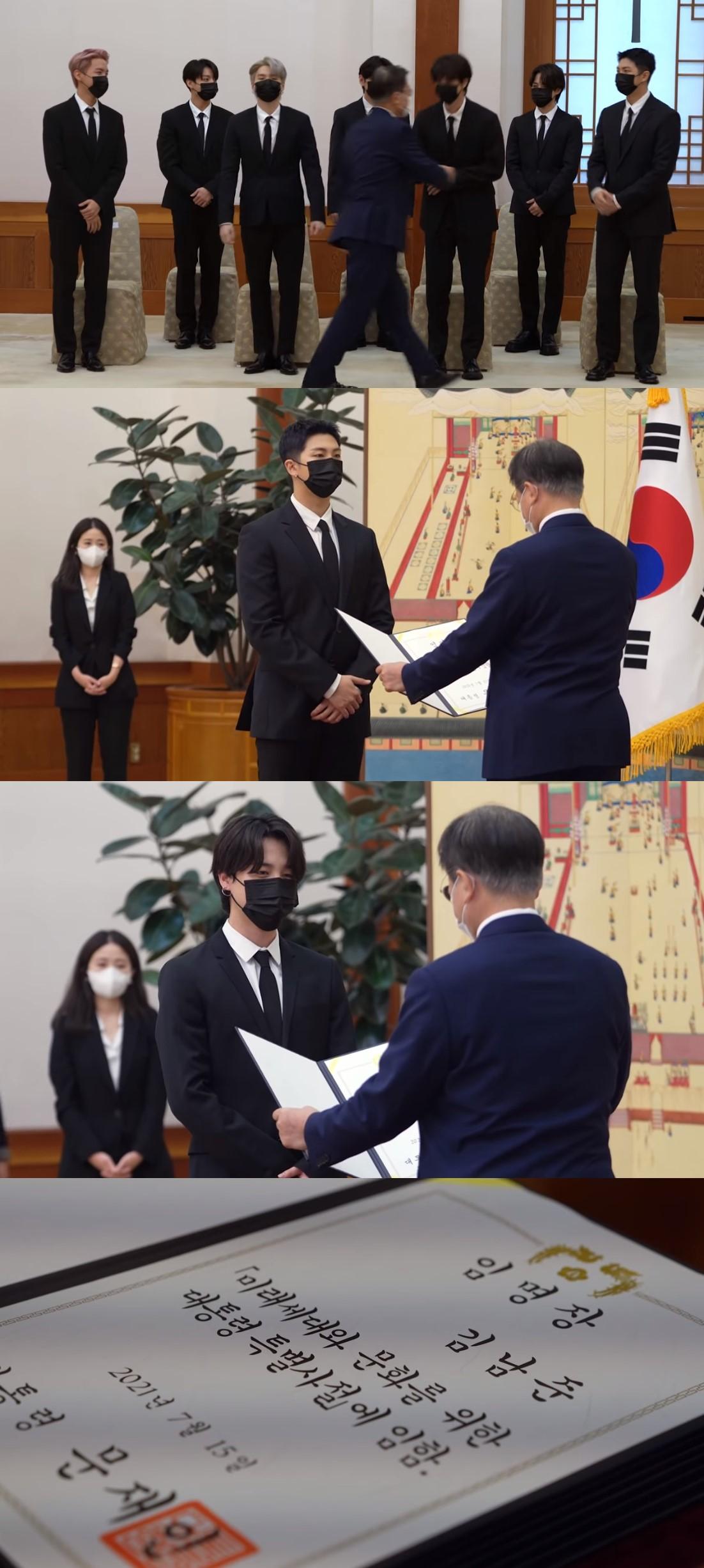 BTSメンバーが大統領から特別使節の任命証を授与される様子。メンバーは黒いスーツを着ている。任命証には『未来世代と文化のための大統領特別使節に任命』と書かれている。