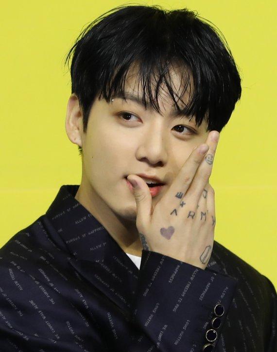 BTSのジョングクが着用しているブラックのスーツ。鮮やかなイエローの背景。ジョングクの手にはハート型のタトゥーが見える。