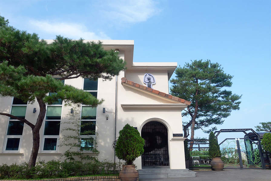 石砌庭院和樹木環繞的九峰山咖啡館入口,建築物外觀為白色小樓房,入口處有黑色鐵門,是一個舒適的環境