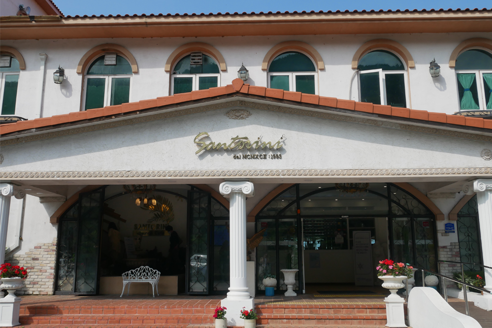 聖托里尼餐廳正面視圖,入口處有門廊和熱帶植栽,營造出希臘風景象