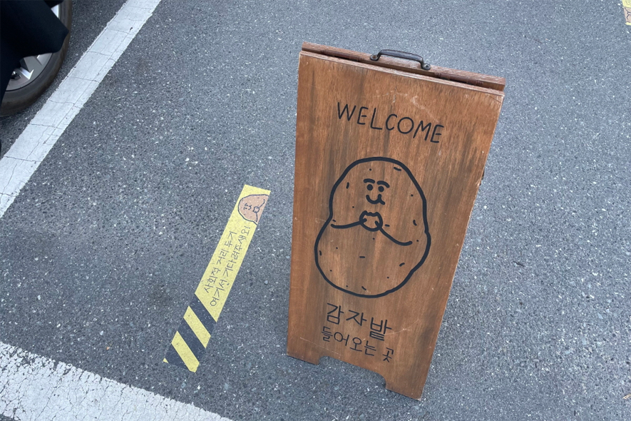 马铃薯田咖啡厅入口处的欢迎标牌，上面有卡通马铃薯娃娃图案，具有独特的招待氛围。