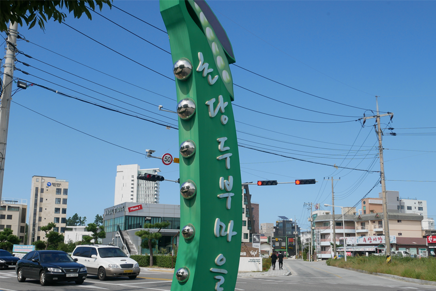 雙語招牌標示 '초당순두부 마을', 站在路邊，背景是城市景觀。