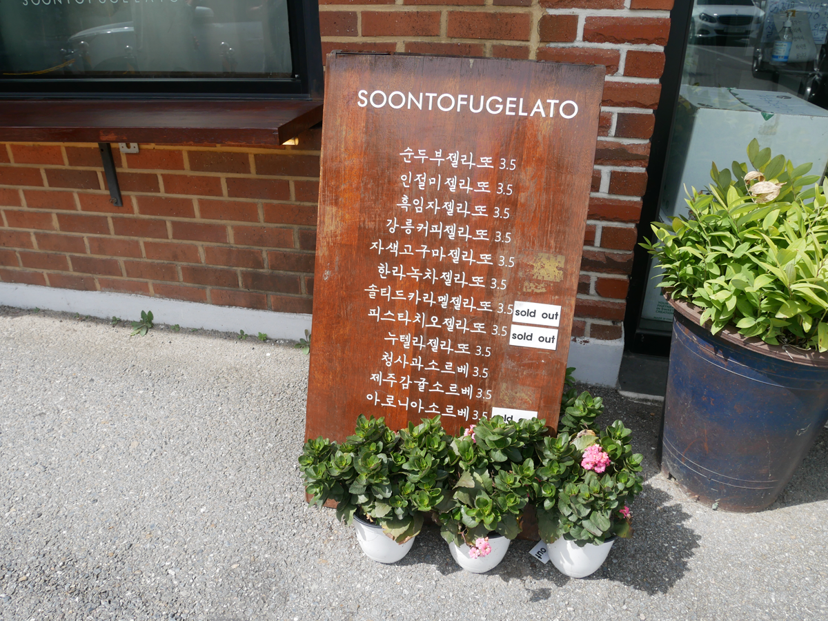 手繪風格的餐牌，描述不同冰淇淋口味，外部放置在 'SOONTOFUGELATO' 商店前。