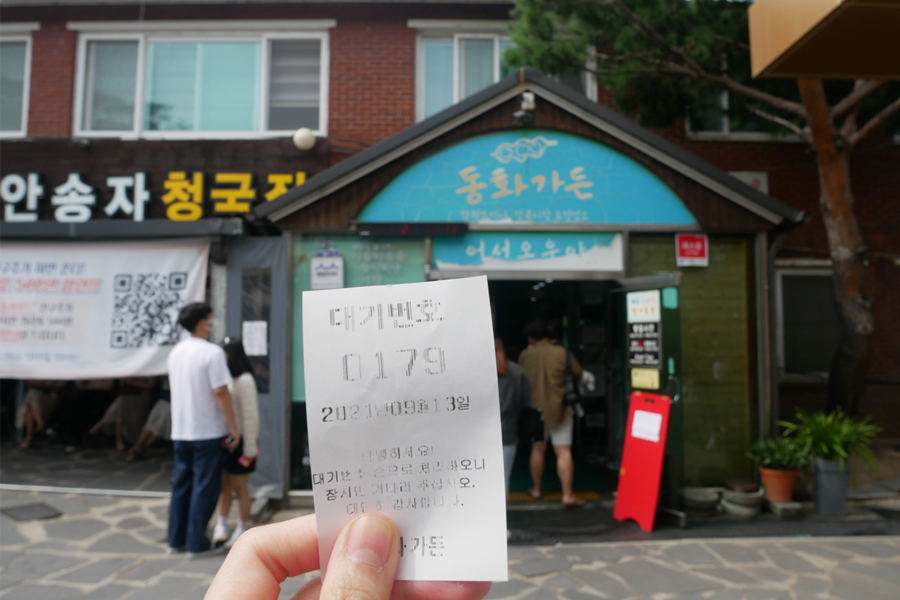 在韓國 '童話花園' 前揮著號碼牌的手，背景是餐廳入口。