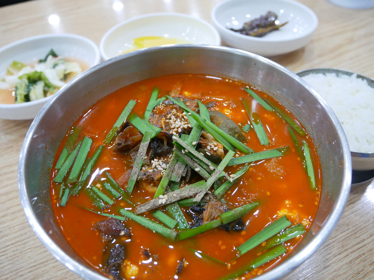 一大碗紅辣海鮮嫩豆腐湯，伴隨著配菜和米飯。