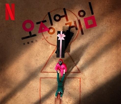 Netflixシリーズ『イカゲーム』の公式ポスター。鍵穴形のコートに、ピンクの制服と緑のジャージを着たキャラクターが描かれている。