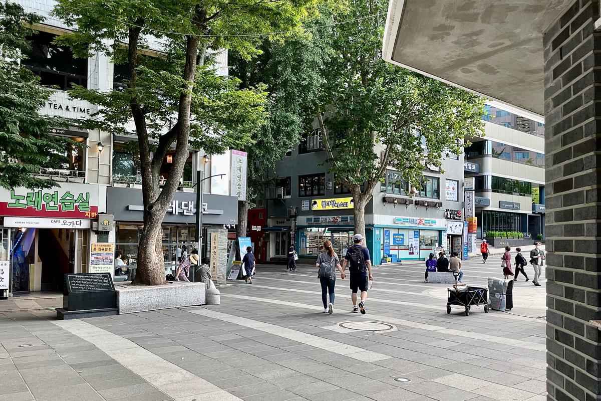 Carrefour animé menant à la rue Insadong à Séoul, avec des gens marchant et des grands arbres le long de la route.