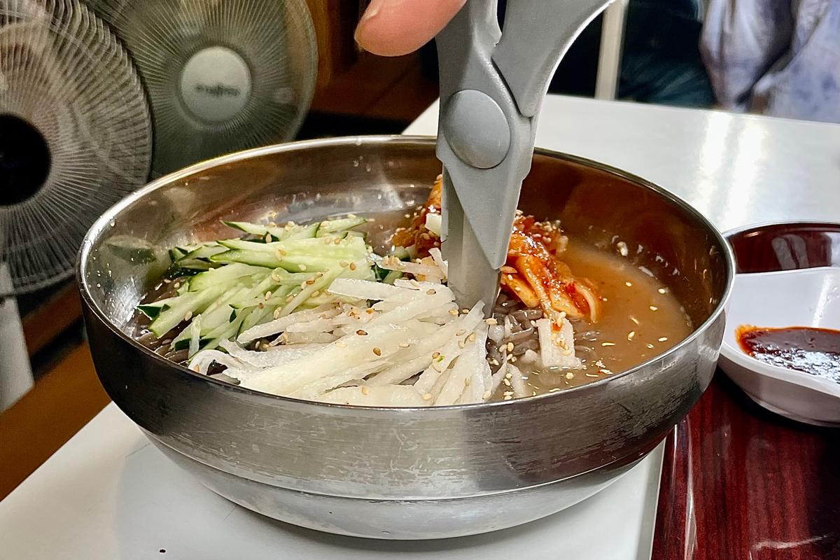 Un membre du personnel du snack-bar coupant et mélangeant les nouilles de sarrasin dans l'eau de radis, offrant un service attentionné.