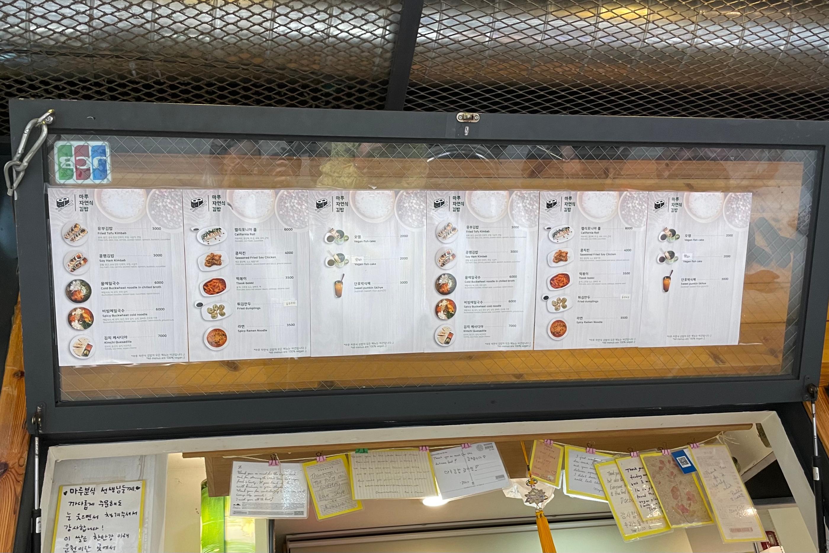 Menu vegan du snack-bar Maru JaYeonSik Kimbap à Insadong, Séoul, affiché sur un panneau avec des plats coréens illustrés.