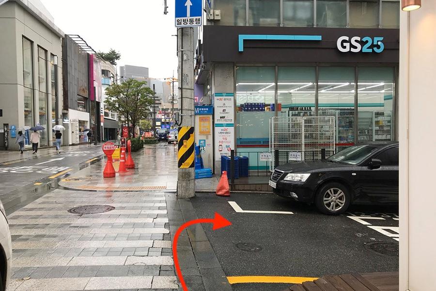 ภาพถนนแนวตรงที่มีอาคารร้านค้าอยู่ทั้งสองข้างที่ภายในเมืองโซล คนเดินไม่หนาแน่นและสภาพอากาศเป็นวันฝนตกเบา ๆ อาคารมีป้ายภาษาเกาหลีและอังกฤษ