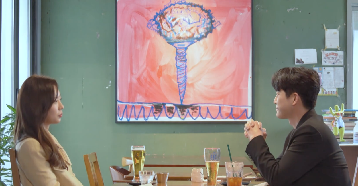 兩人在首爾的餐廳，桌上擺滿了美食和飲料，背景有綠色牆壁，牆上掛有色彩鮮豔的藝術畫作。