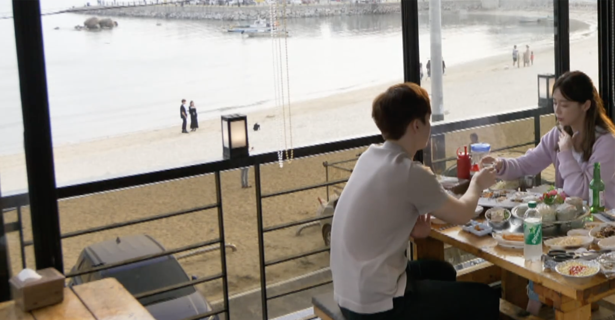 海邊餐廳的玻璃窗外是美麗的沙灘風景，海天一色，適用於放鬆休閒的氛圍場景。