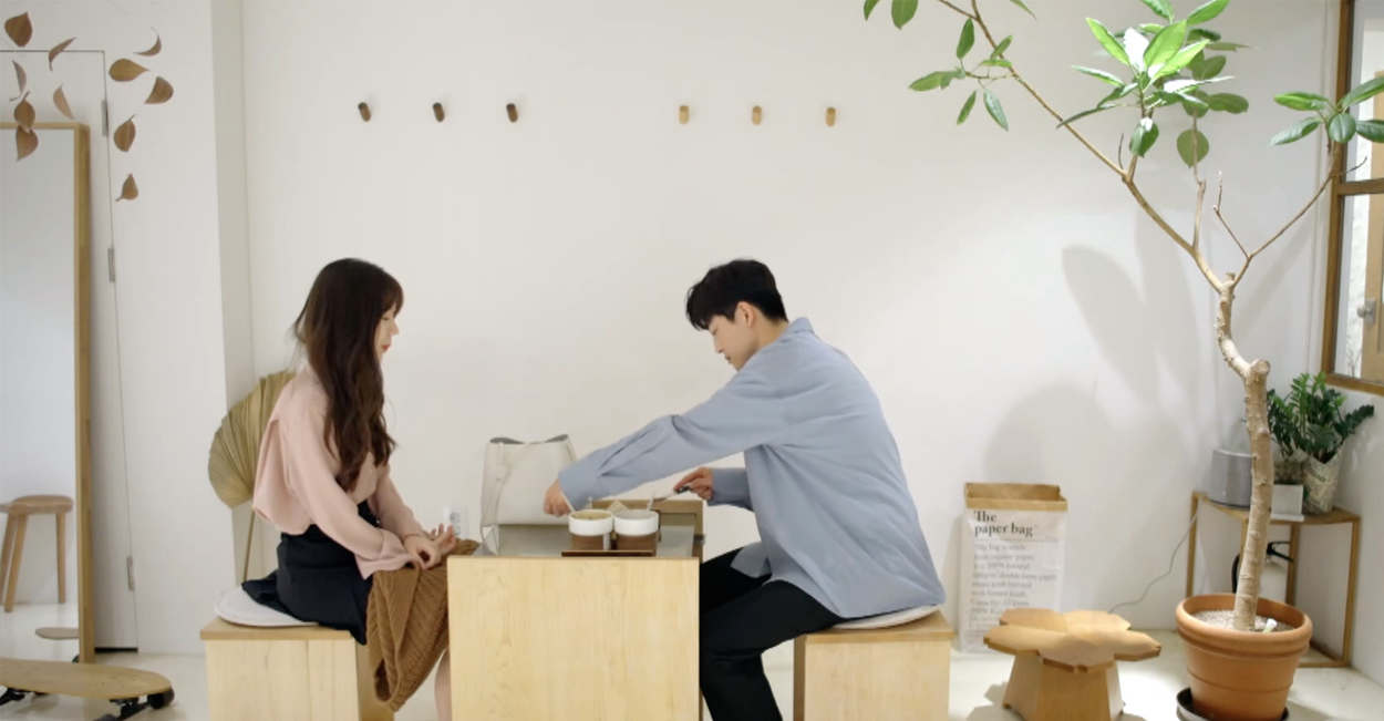 韓式咖啡館的窗邊座位，綠色樹葉映襯，窗外是模糊的城市景觀，氛圍靜謐。